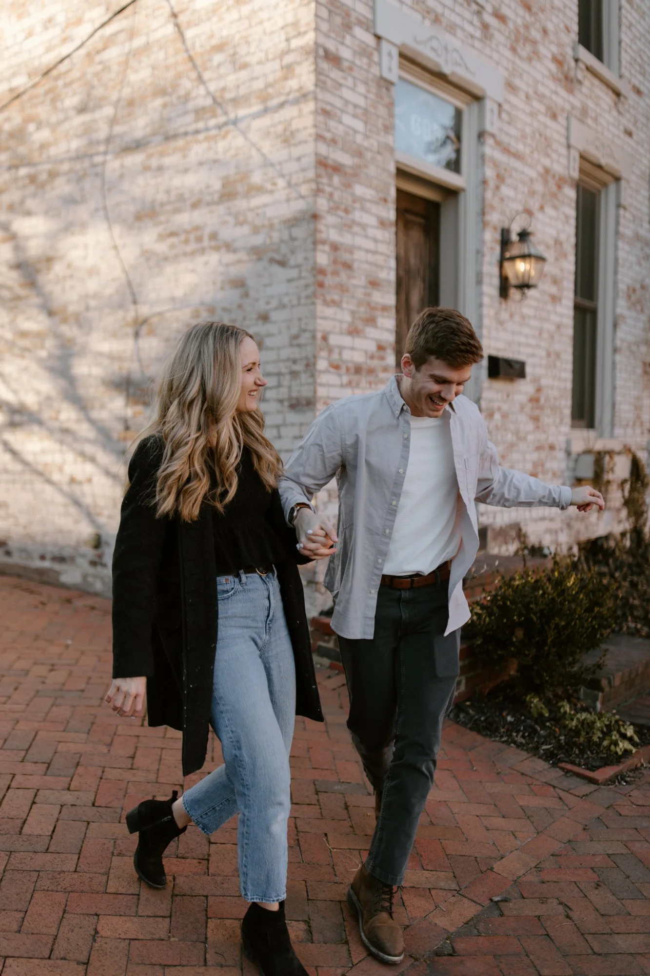 A couple laughing as they walk hand in hand past a brick building