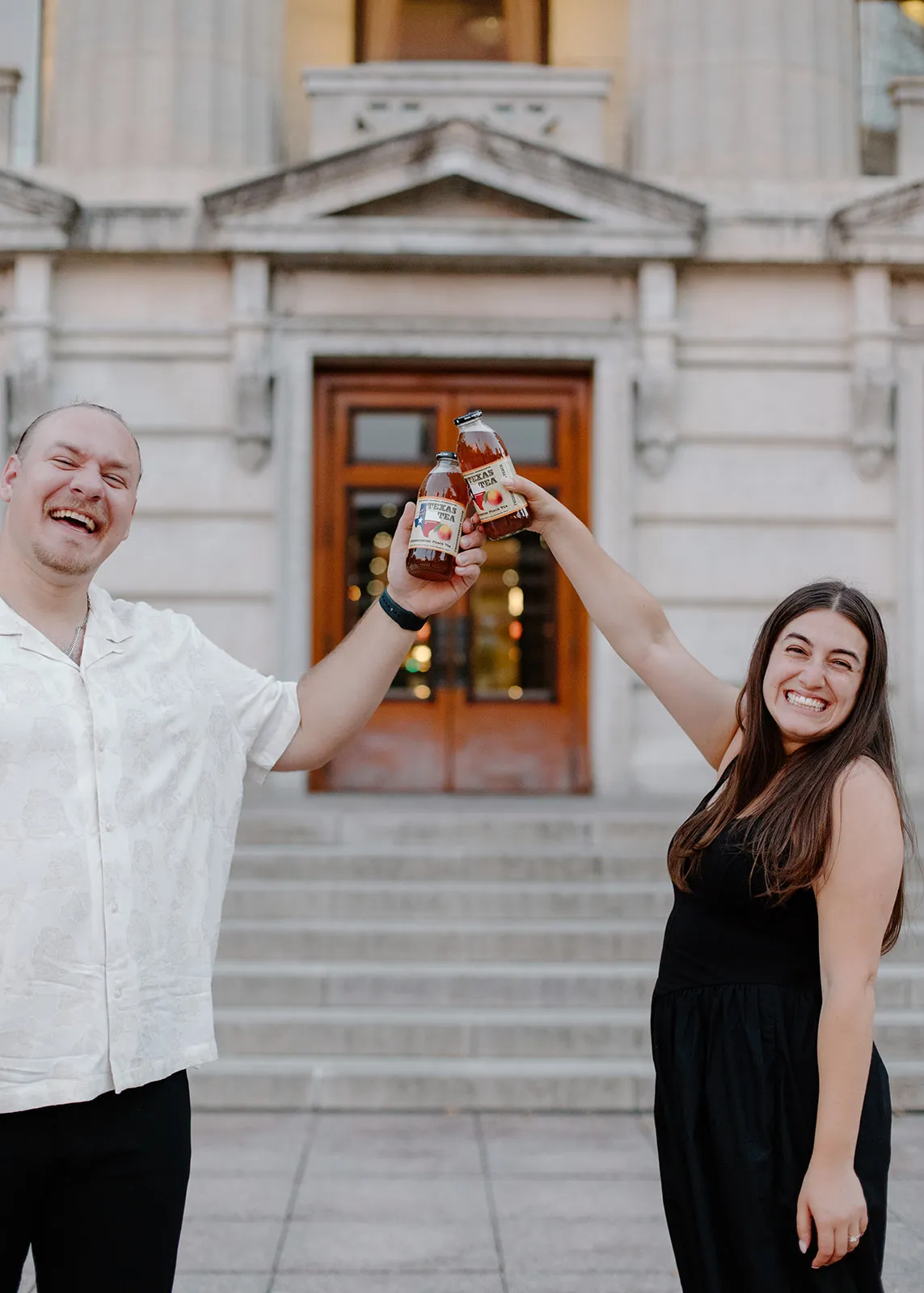 Gina and Jacob toasting with bottles of peach tea on the steps
