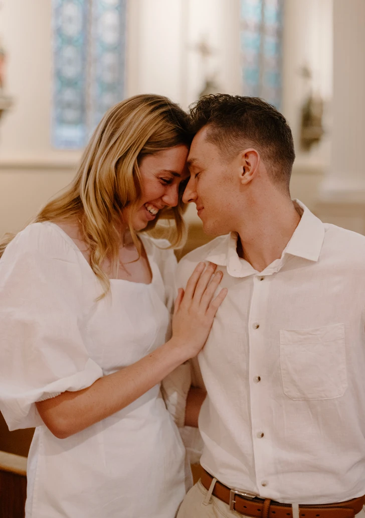 Gerrin and Meredith forehead to forehead in a church, her hand on his chest, both smiling
