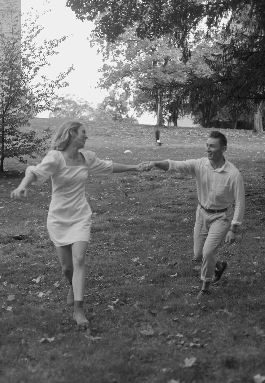 Black-and-white of the couple running hand in hand across a park lawn