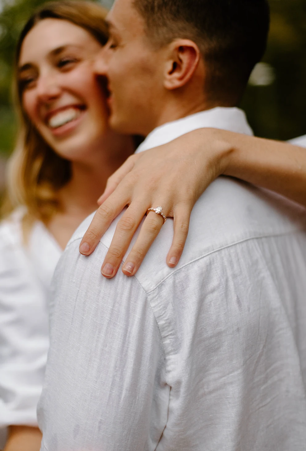 Her ring hand on his shoulder, her laughing face soft in the background
