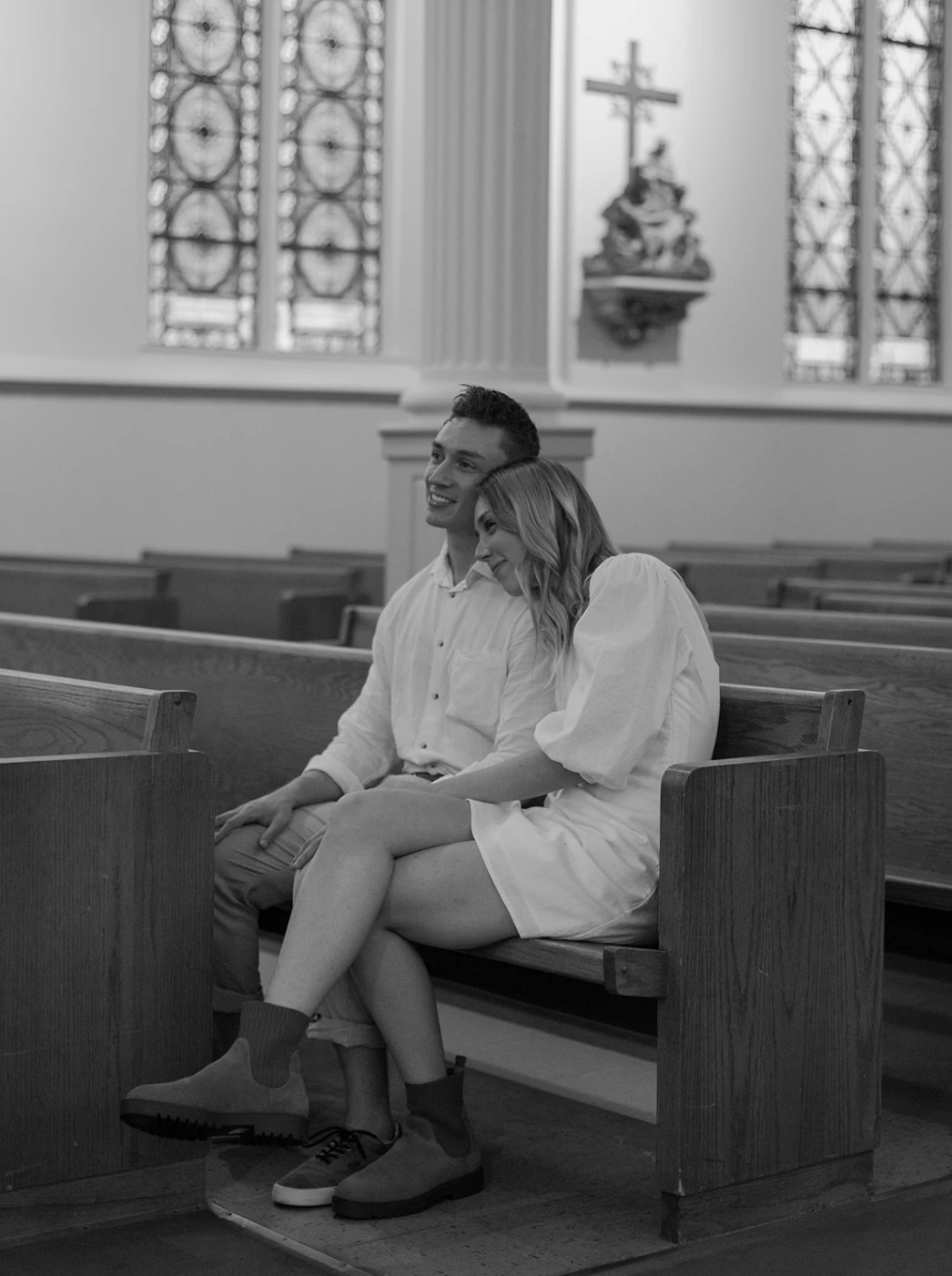 Black-and-white of the couple sitting in a church pew, her head on his shoulder