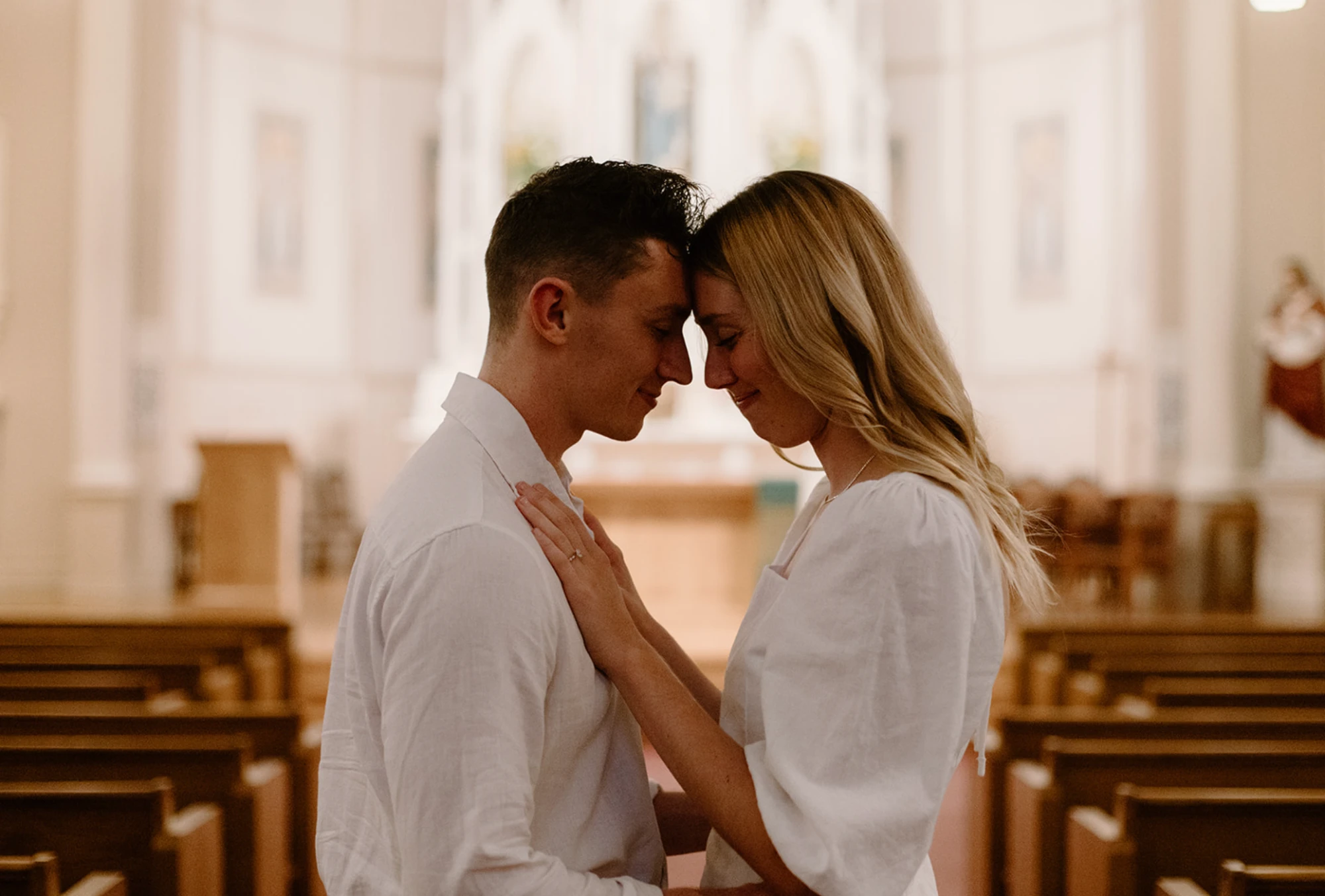 The couple forehead to forehead in the church aisle between rows of pews