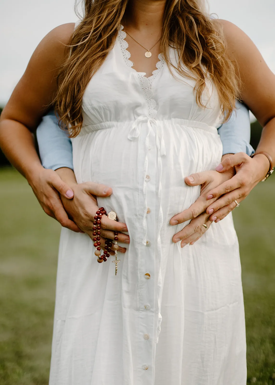 Their hands on her belly, holding a rosary