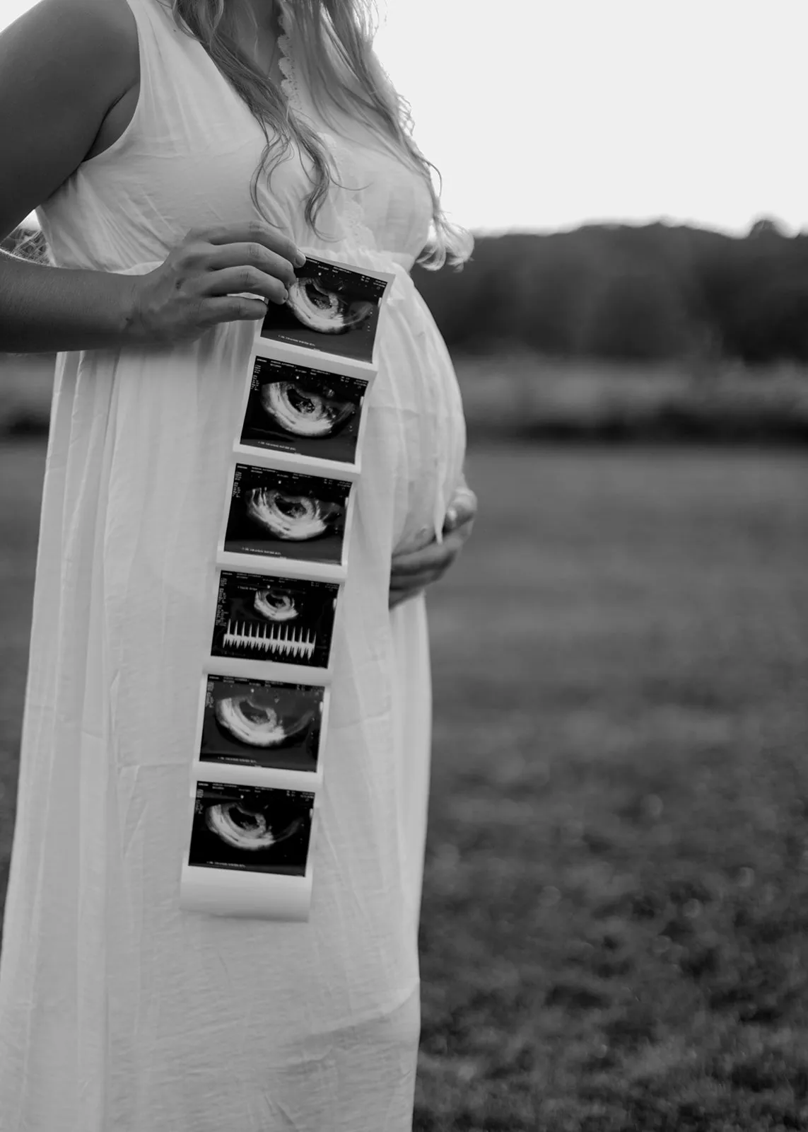 Black-and-white of her holding a strip of ultrasound photos beside her belly