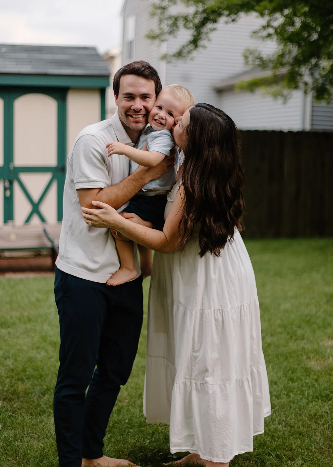 Mom and dad squeezing their son between them for a kiss in the yard